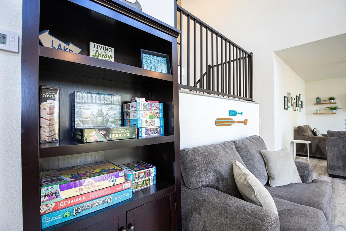 A cozy nook featuring a comfortable couch, a bookshelf filled with board games, and decorative paddles on the wall. This friendly setup is clearly designed for relaxed family game nights or casual conversations, with inviting textures and whimsical decor.
