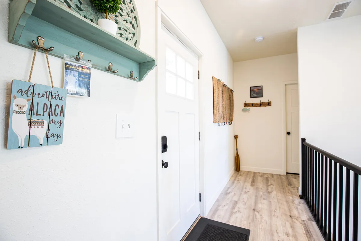 This image captures an inviting entryway featuring a welcome door, a playful adventure alpaca sign, decorative hooks, and a planter shelf. The door is a likely location for smart locks or video doorbells.