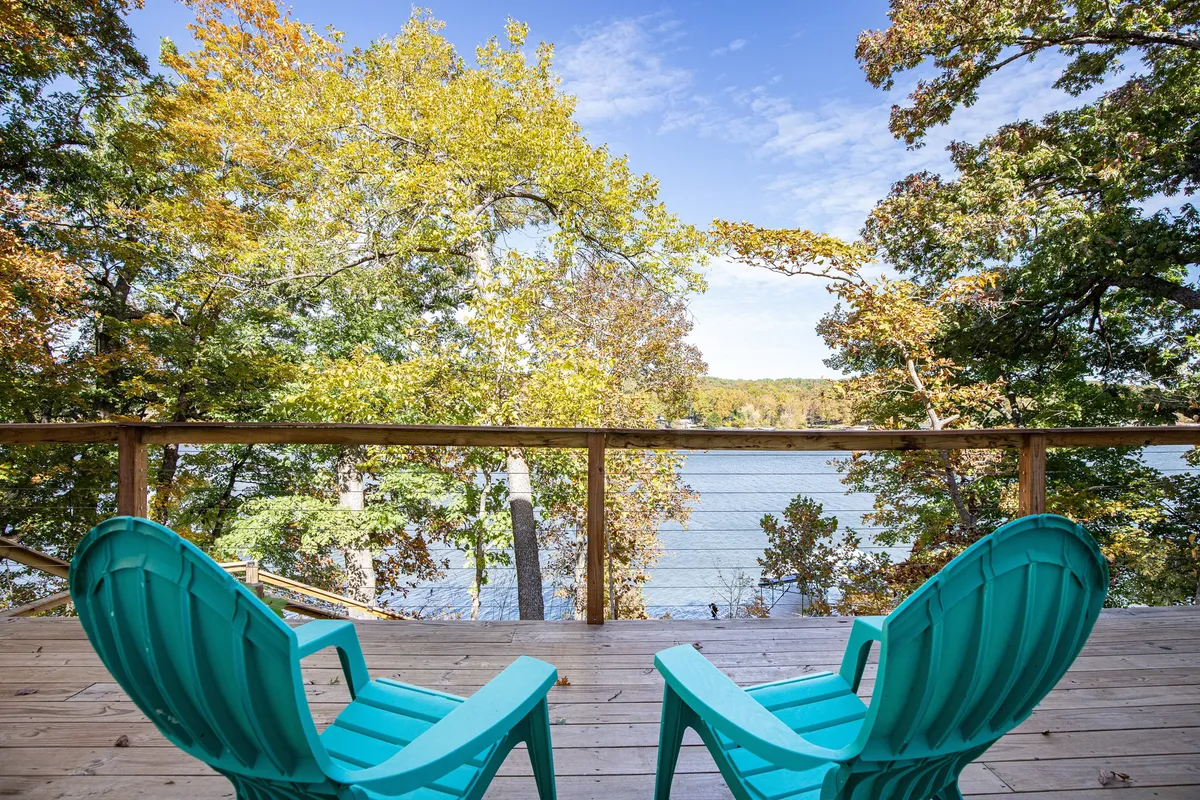 A pair of turquoise chairs are positioned to overlook the sparkling lake, framed by surrounding trees, inviting guests to relax, read, or enjoy the peaceful scenery. The setting radiates quiet and serenity, with the lake view as the focal point.