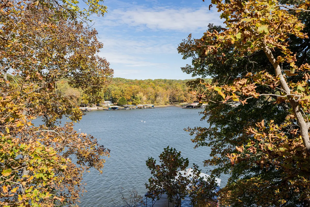 A picturesque view over the lake framed by vibrant autumn foliage, with boathouses in the distance and gentle hills rolling along the horizon. The serene water invites boating, fishing, or simply enjoying the scenery. The golden hour lighting adds warmth and tranquility to the scene.