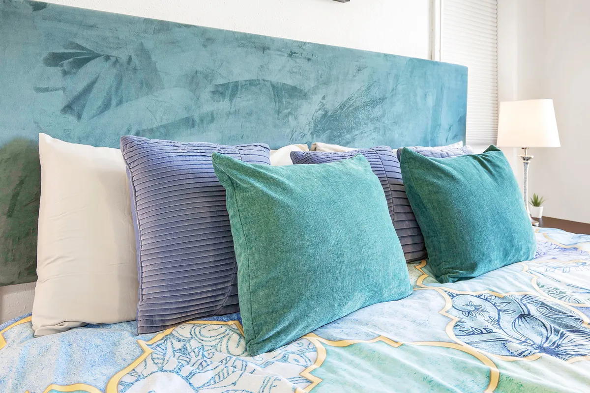 An inviting bedroom with a teal headboard, plush pillows, and a decorative bedspread. The atmosphere is serene, perfect for peaceful evenings or quiet afternoons spent reading and relaxing.