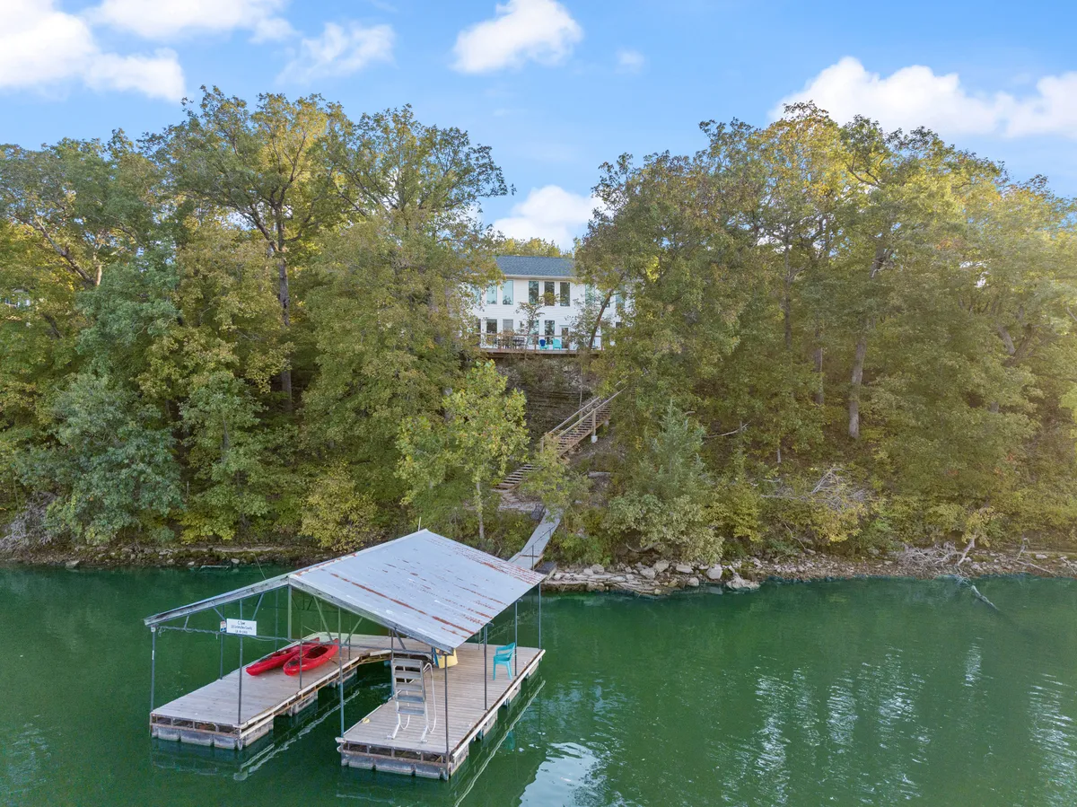 This image captures a serene lakeside scene with a private dock extending over the water. Several brightly colored kayaks rest on the dock, and the house is visible close by among the trees, emphasizing the proximity of the water to the accommodation. The environment is tranquil and inviting, highlighting both relaxation and outdoor adventure possibilities.
