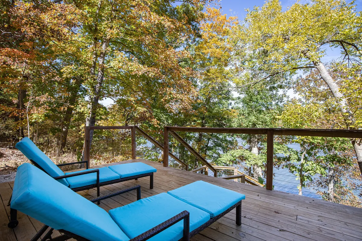 This image features inviting blue lounge chairs placed on a wooden deck overlooking a serene lake, framed by autumn foliage. The lake view is expansive, and the scene is peaceful, with plenty of space for relaxation and outdoor companionship.