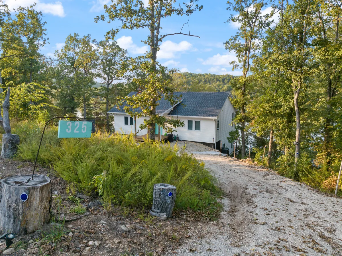 The exterior of the house is shown, with its welcoming sign, driveway lined with trees, and abundant greenery. There’s a sense of arrival and connection to nature, with ample space around the home for walking and outdoor play.