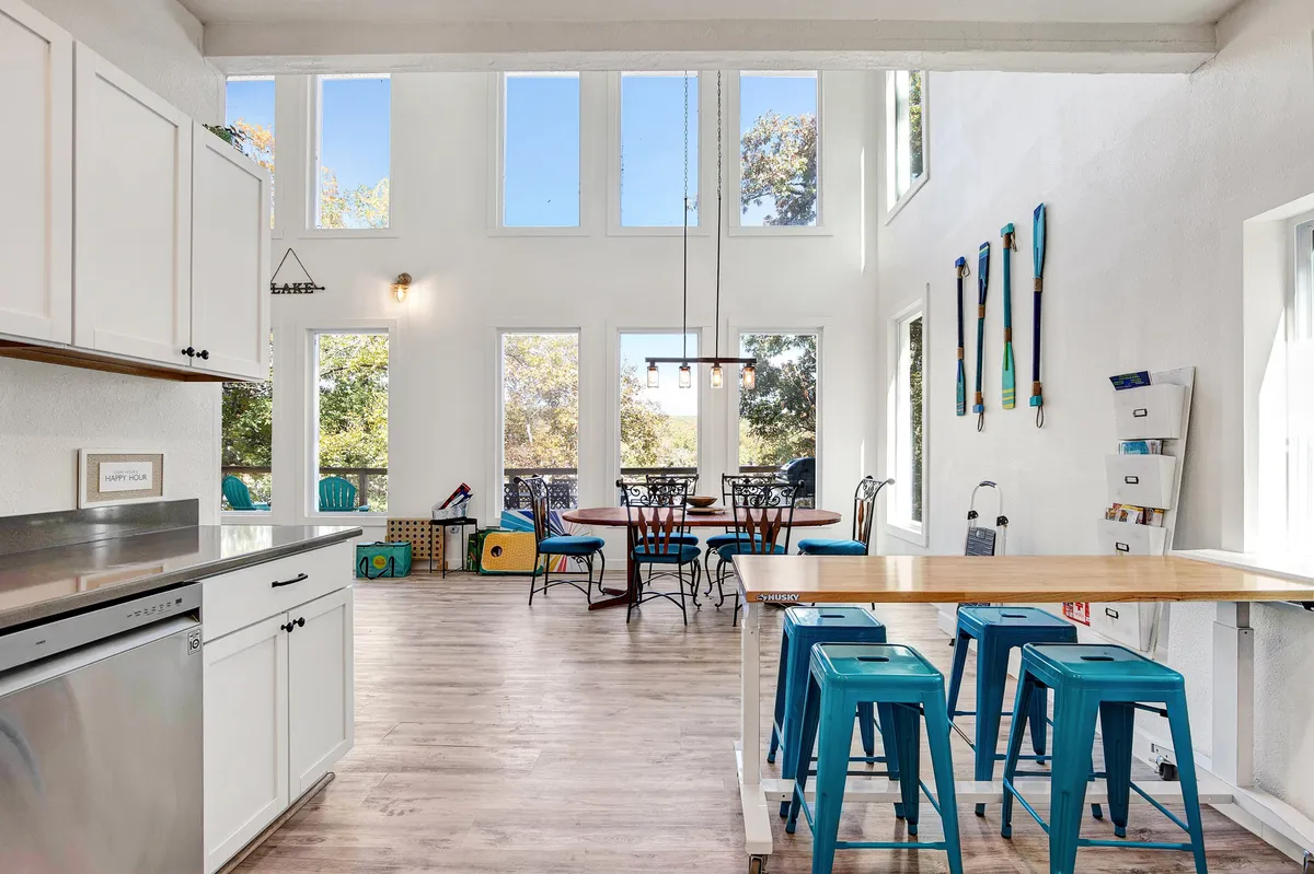 An open-concept kitchen with a large island, adjacent dining table, and big windows offering serene views. Decorative paddles on the wall add a lakeside touch. The setting is relaxed and cheerful, perfect for gathering and sharing meals.